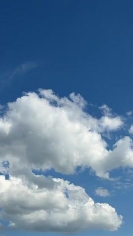 The video shows a bright blue sky dotted with fluffy white cumulus clouds.