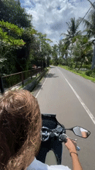 Two people ride scooter through Ubud under cloudy skies