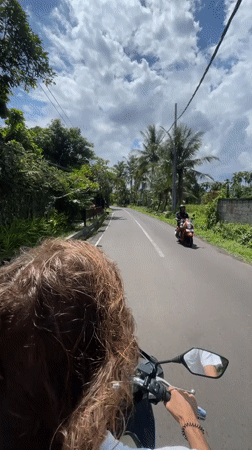Two people ride scooter through Ubud under cloudy skies