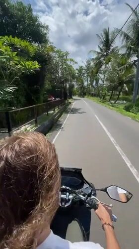 Two people ride scooter through Ubud under cloudy skies