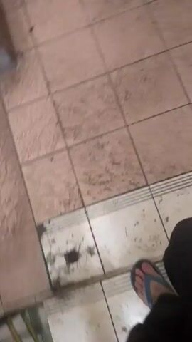 The video shows a person walking on a dirty, tiled floor and up a set of tiled stairs. The tiles are a light brown color and have dark smudges on them. The person is wearing sandals. A handrail is visible on the left side of the stairs.