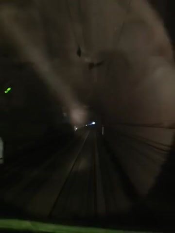 A fisheye lens view from inside a train car shows a dark tunnel with illuminated train tracks ahead. The walls of the tunnel are visible, and there are lights along the tracks. The train appears to be moving at a high speed, as indicated by the motion blur. The video is less than five seconds long.