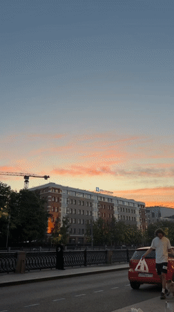 Man observes small dog near red car at urban dusk