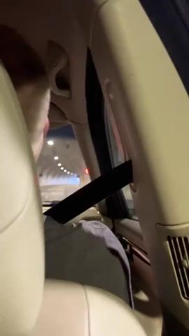 The media file shows the interior of a car, as viewed from the back seat. A person wearing a grey shirt is visible in the foreground, partially obscured by the car's interior. A black seatbelt is stretched across the frame, diagonally from the upper right to the lower left.

Through the car window, a tunnel with numerous lights is visible. The lights suggest that it is nighttime or that the tunnel is poorly lit. The car appears to be moving through the tunnel, indicated by the sense of motion and the receding lights.

There is no visible text in the media file. The setting appears to be a road tunnel, likely in Kongsberg, Norway, based on the provided location context. The overall mood is one of travel and transition through a dark, enclosed space. The bright lights of the tunnel create a contrast with the dim interior of the car.