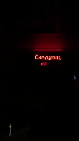 The camera is still and directed at a digital display inside a bus or similar vehicle, showing the time, the bus route number (133), and cycling Russian text that translates to "Next stop". The display is bright red against a dark background, and the lighting is dim.