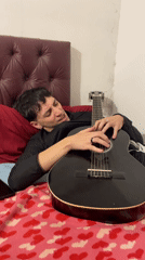 Young man plays acoustic guitar on bed in Buenos Aires