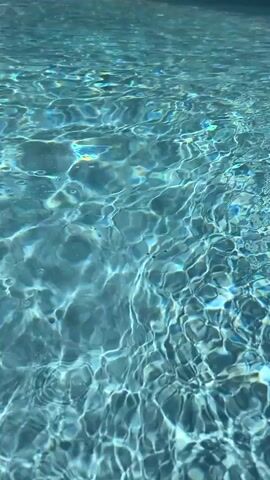 The video shows a close-up of clear blue pool water. The surface of the water is rippled and reflects light, creating a shimmering effect. There are no people or objects visible in the frame, only the water. The lighting suggests it is daytime.