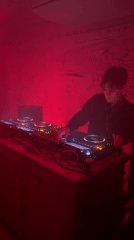 DJ performs in red-lit graffiti room with mixing equipment