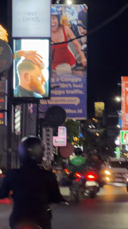 Motorcyclist rides through North Kuta street traffic amid illuminated signs