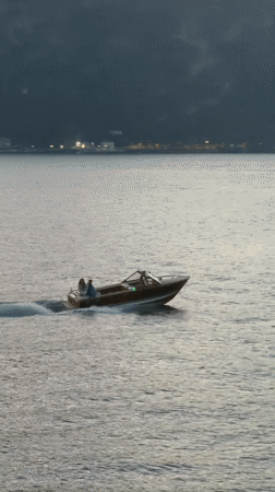 Motorboat crossing calm alpine lake at dusk, Como region