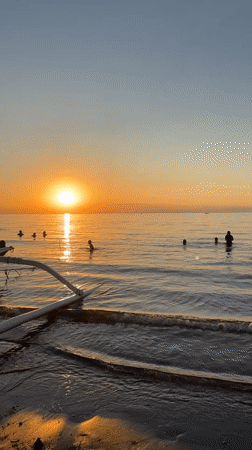 Golden sunset scenes captured along Bali coast with swimmers, boats