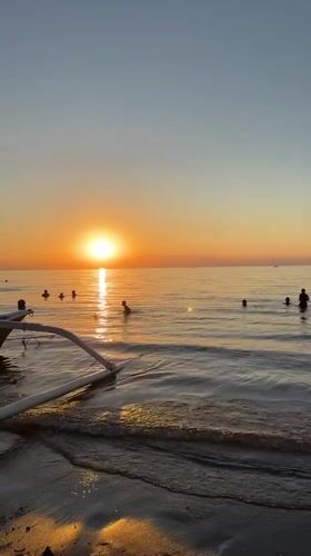 Golden sunset scenes captured along Bali coast with swimmers, boats