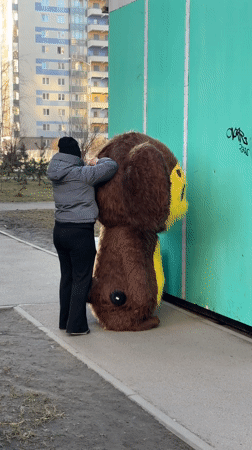 Person assists costumed figure on Kudrovo sidewalk