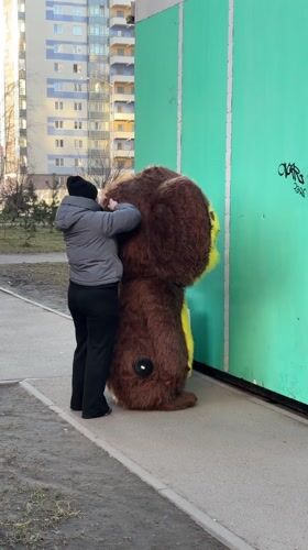 Person assists costumed figure on Kudrovo sidewalk