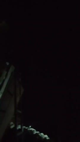 A dark video shows a person talking about stars. The person appears to be outside at night and is pointing to the sky. There are some lights visible in the distance. The person is excited and points out what they believe to be stars.