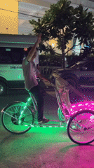 Rickshaw operator waves from LED-lit bicycle in Vietnam