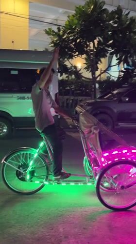 Rickshaw operator waves from LED-lit bicycle in Vietnam