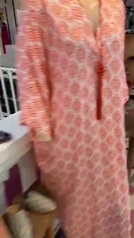 The video shows the interior of a clothing store. The floor has a patterned tile design in pink and white. The store appears to have a variety of clothing items on display, including dresses on hangers and shelves with accessories. The store is well-lit and seems to be located in a shopping mall or similar complex, as suggested by the presence of other shops visible through the store's open front. The video ends with a shot of a closed white rolling shutter.