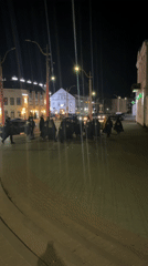 Hooded figures walk cobblestone street in Hrodna at night