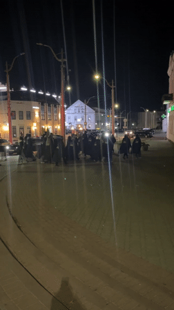 Hooded figures walk cobblestone street in Hrodna at night
