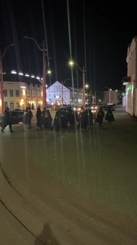 Hooded figures walk cobblestone street in Hrodna at night