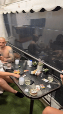 Social gathering observed around cluttered patio table in Nea Peramos