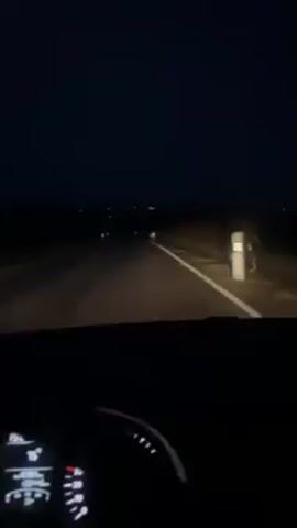 The video shows a car driving on a dark, rural road at night. The car's headlights illuminate the road ahead, which is marked with white lines. The dashboard of the car is visible, showing the time as 19:24 and a fuel level indicator. There are also some lights in the distance. A song can be heard playing.