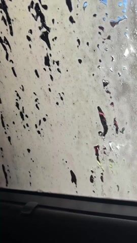 The video shows the interior view from inside a car as it goes through an automated car wash. Initially, the windshield is covered in streaks and splotches of white foam with red streaks. These are then washed away by horizontal streams of soap and water. The view is limited to the front windshield of the car.