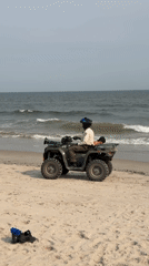 ATV rides the shoreline as beachgoers swim near a breakwater