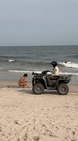 ATV rides the shoreline as beachgoers swim near a breakwater