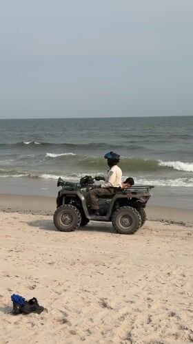 ATV rides the shoreline as beachgoers swim near a breakwater