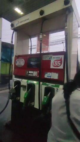 Here is a detailed description of the video:

The video shows a close-up of a gas pump at a Pertamina gas station. Pertamina is an Indonesian state-owned oil and natural gas corporation. The pump has three nozzles labeled "Bio Solar," "Dexlite," and "Pertamina Dex." A Pertamina Call Center sign is prominently displayed. The lighting is overcast, and the overall environment suggests a typical day at a gas station. A truck is partially visible in the background, and the scene is situated along a road with power lines overhead.