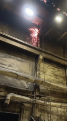 Sparks fly overhead in a factory, with a tree canopy break