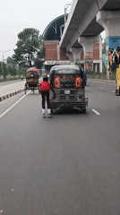 Person roller skates behind auto-rickshaw on busy Dhaka street