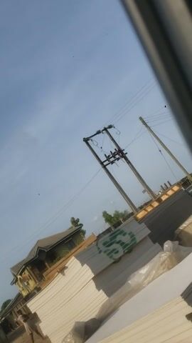 The view is tilted upwards, showing power lines and poles against a blue sky. A stack of white panels, possibly construction materials, is visible to the right, and a building with a dark roof is partially visible in the lower right corner. The camera angle suggests the view is from a low vantage point.