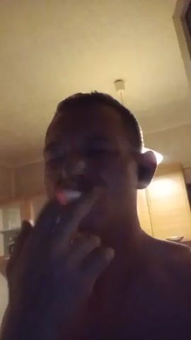 The video shows a close-up of a person smoking a cigarette. The person's face is mostly in shadow, but their eyes are closed and their hand is holding the cigarette. The cigarette is lit, and smoke is visible. The background appears to be an indoor setting with cabinets and a ceiling light. The video is shaky and appears to be self-recorded.
