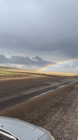 Double rainbow appears over wet rural Russian road