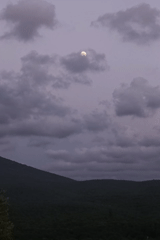 Full moon rising over forested hills and dry meadows at dusk