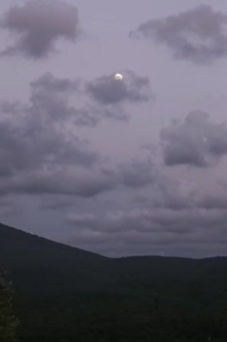 Full moon rising over forested hills and dry meadows at dusk