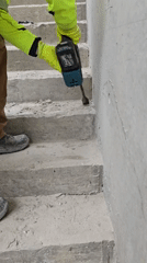 Construction worker chips concrete on staircase with power tool