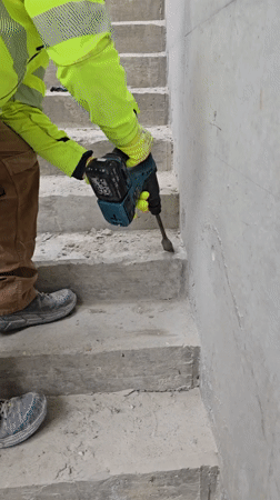 Construction worker chips concrete on staircase with power tool