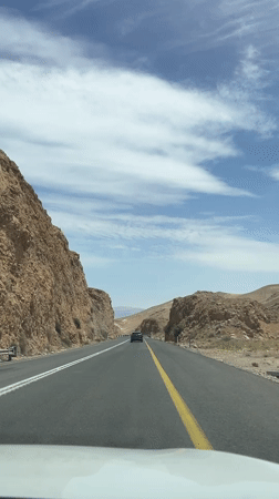 Car travels desert canyon road near Arad on sunny day
