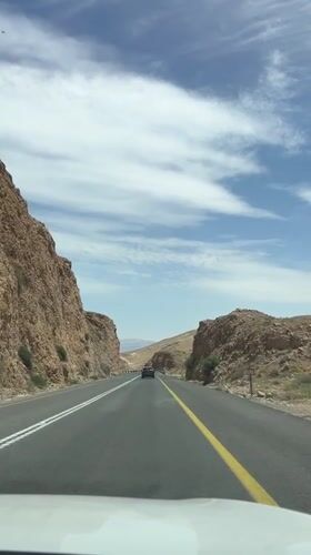 Car travels desert canyon road near Arad on sunny day