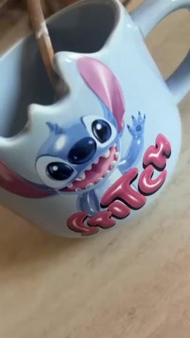A close-up video shows a blue mug with a Stitch character design. A spoon is shown in the mug, partially filled with yogurt and chia seeds. The video is a close-up shot of the yogurt and chia seeds in the mug. The mug is light blue with a cartoon drawing of Stitch on it. The spoon is silver and has some yogurt on it. The chia seeds are dark brown and are scattered on top of the yogurt.
