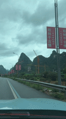 Car drives past red banners, sculpture in Guilin hills