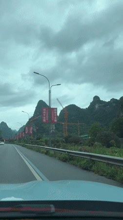 Car drives past red banners, sculpture in Guilin hills