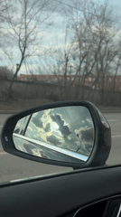 Car mirror reflects cloudy sky during drive in Krasnoyarsk