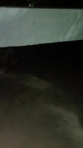 This extremely dark and blurry video shows an indistinct, likely outdoor or dimly lit indoor scene. The dominant colors are shades of dark grey and brown. A lighter, blurry grey/white horizontal band is briefly visible at the top of the frame in the initial seconds, possibly indicating a ceiling or an overhang. The majority of the video consists of blurred, dark grey and brown shapes, which appear to be ground or a floor, with some faint, undefined textures. The camera is in motion throughout the clip, causing significant motion blur and making any specific objects or details unidentifiable. The time of day is clearly dark, suggesting night or a very poorly lit environment. No people, specific objects, or discernible text are visible. There are no visual cues within the video to confirm the provided location context of Tahlequah, United States of America.