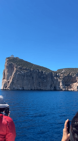Tourist observes cliff island from boat near Alghero