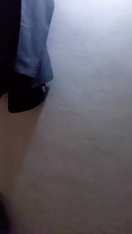 The video shows a grey suit jacket and a dark vest hanging on a white wall, likely in a closet or room. The camera angle shifts slightly, providing a closer view of the clothing. The lighting is somewhat dim, but details like the buttons on the vest and the texture of the suit jacket are visible.